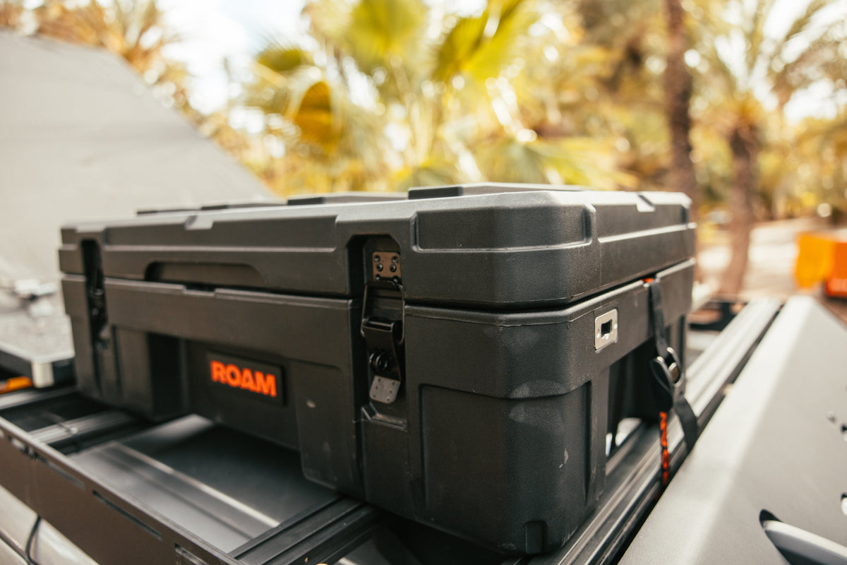 Black ROAM storage box on a vehicle roof with trees in the background