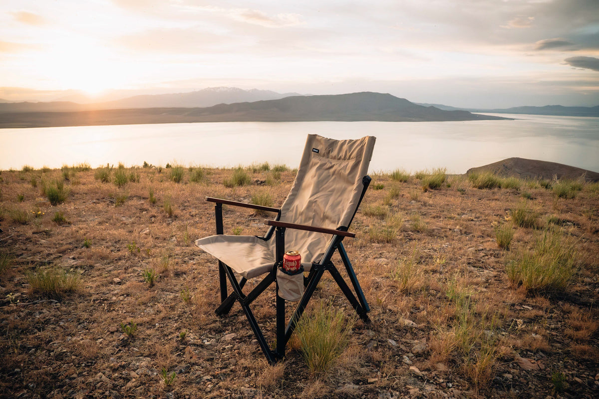 Chair on a grassy hill with a scenic view of a lake and mountains at sunset.