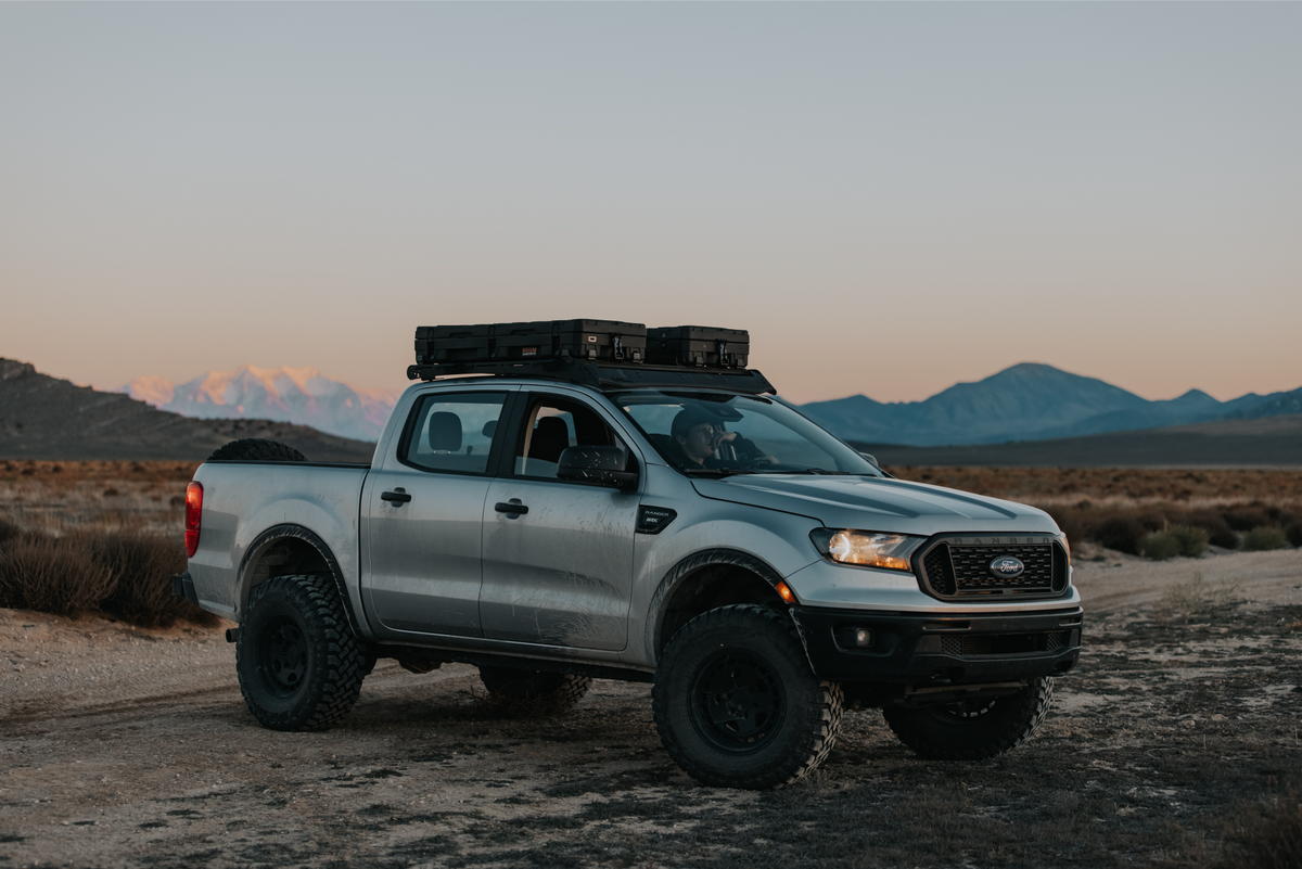 Silver Ford truck with roof rack in a desert landscape at sunset